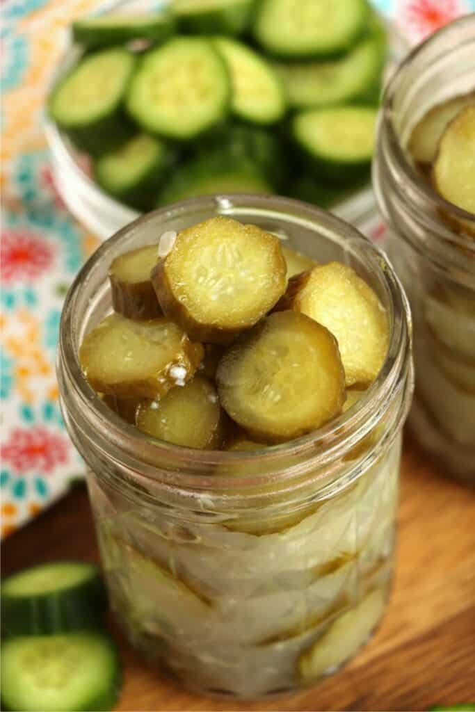 Closeup shot of jarful of homemade horseradish pickles with sliced cucumbers in background. 