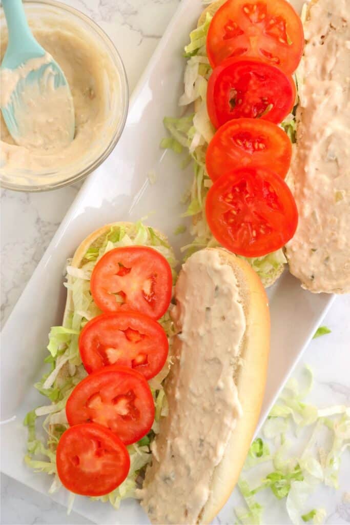 Overhead shot of sub rolls topped with seasoned mayo, lettuce, and tomato