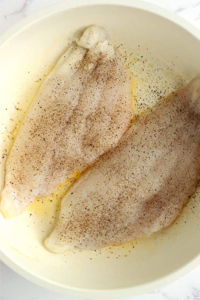 Closeup overhead shot of catfish filets being cooked in a skillet. 