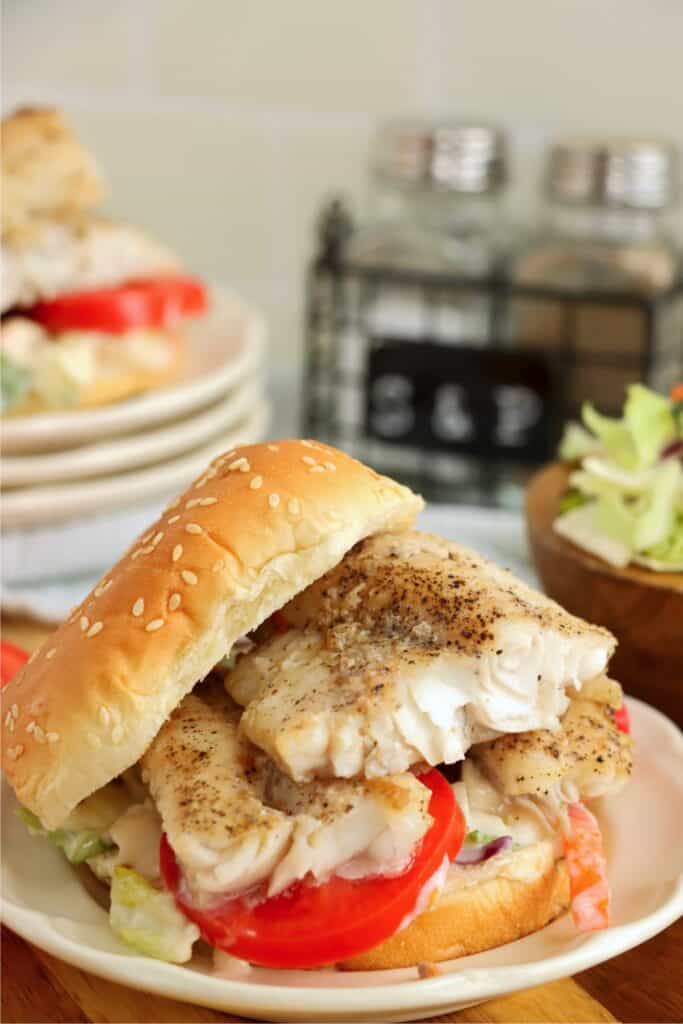 Closeup shot of catfish sandwich with coleslaw, sliced tomatoes, and catfish filet. 