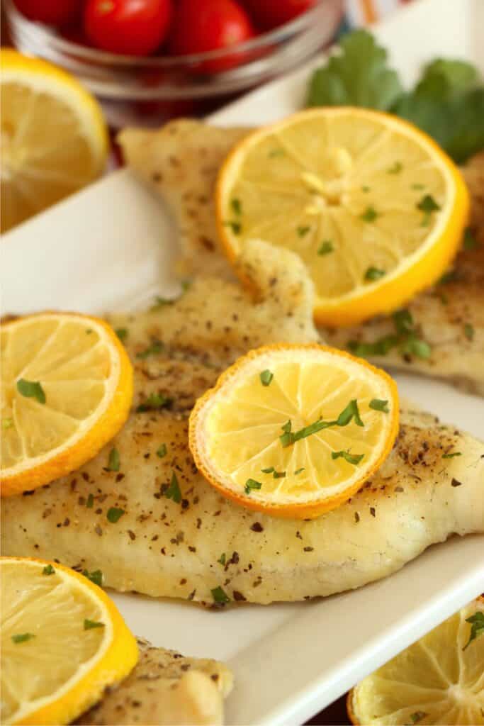 Closeup shot of catfish steaks topped with lemon slices on plate. 