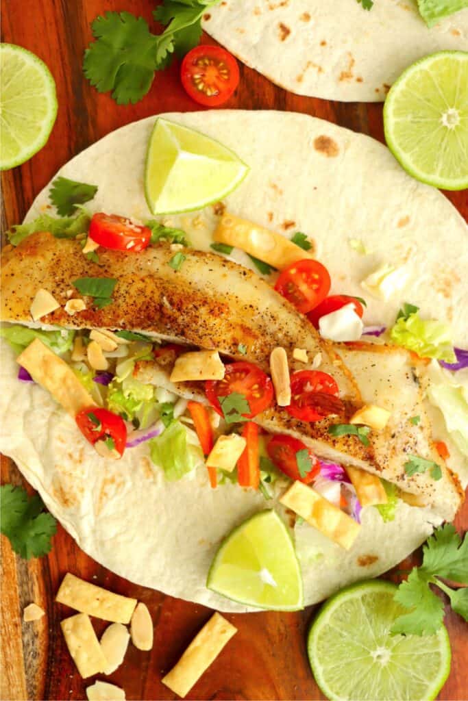 Overhead shot of tortilla topped with catfish, Asian salad, tomatoes, and wonton strips. 