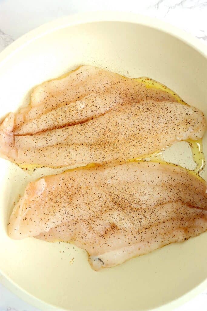 Overhead shot of seasoned catfish filets in skillet with oil. 