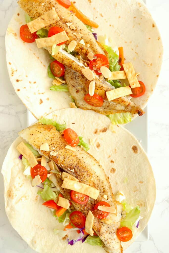 Overhead shot of two catfish tacos with catfish, Asian salad, wonton strips, slivered almonds, and tomatoes.