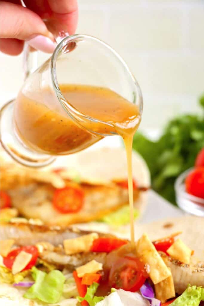 Closeup shot of vinaigrette being drizzled over catfish tacos. 