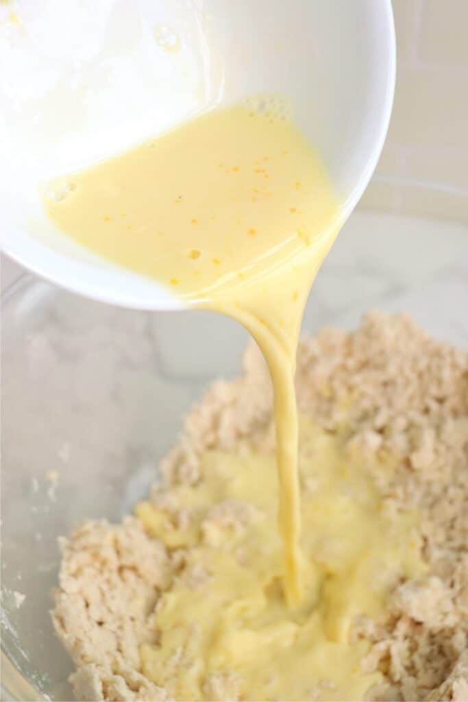 Egg mixture being poured into bowlful of flour and shortening mixture.