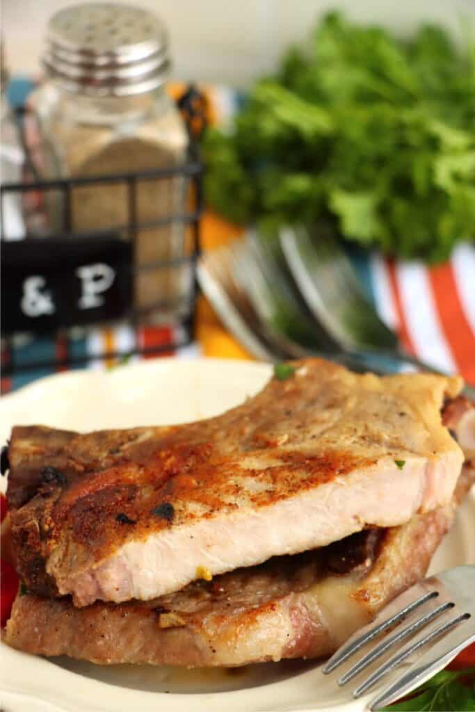 Closeup shot of tow reverse sear pork chops stacked atop one another on plate with to pork chop cut in half. 