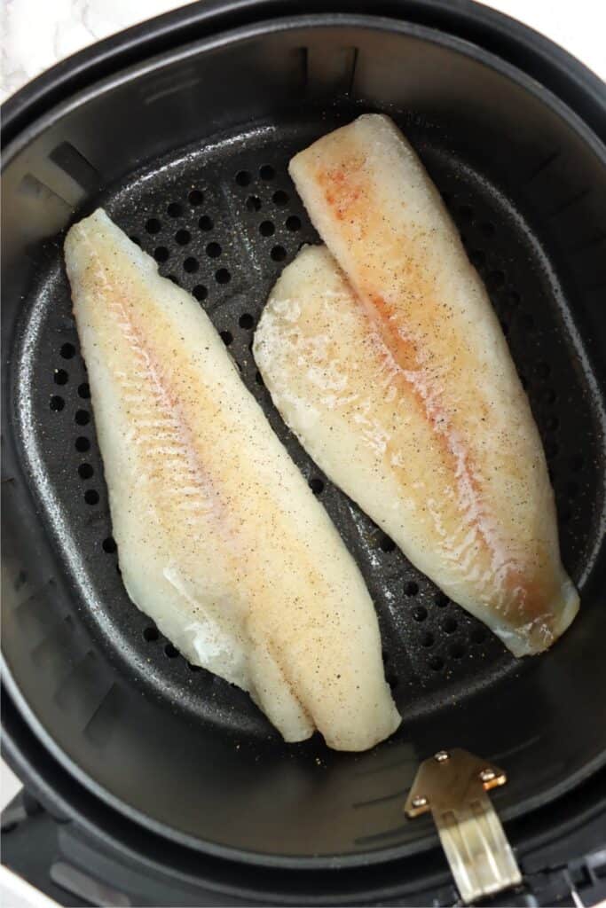 Overhead shot of froze cod fillets in air fryer basket.