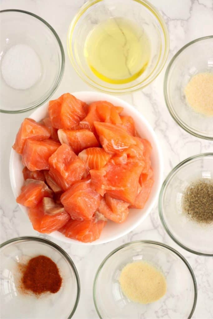 Overhead shot of salmon bite, oil, and seasonings in bowls.