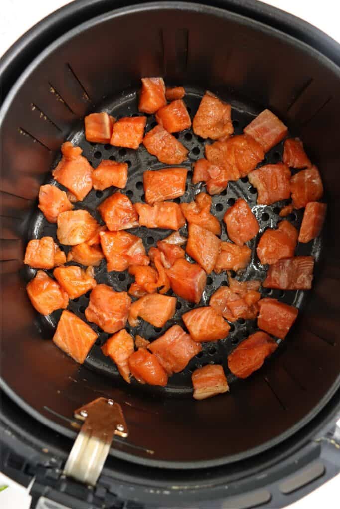 Overhead shot of seasoned salmon bites in air fryer basket. 