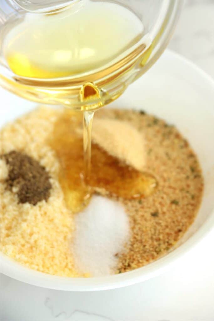 Closeup shot of oil being poured into bowl of breadcrumbs and seasonings.