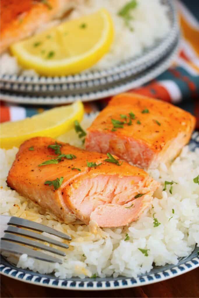 Closeup shot of hot honey salmon fillet cut in half over bed of white rice. 