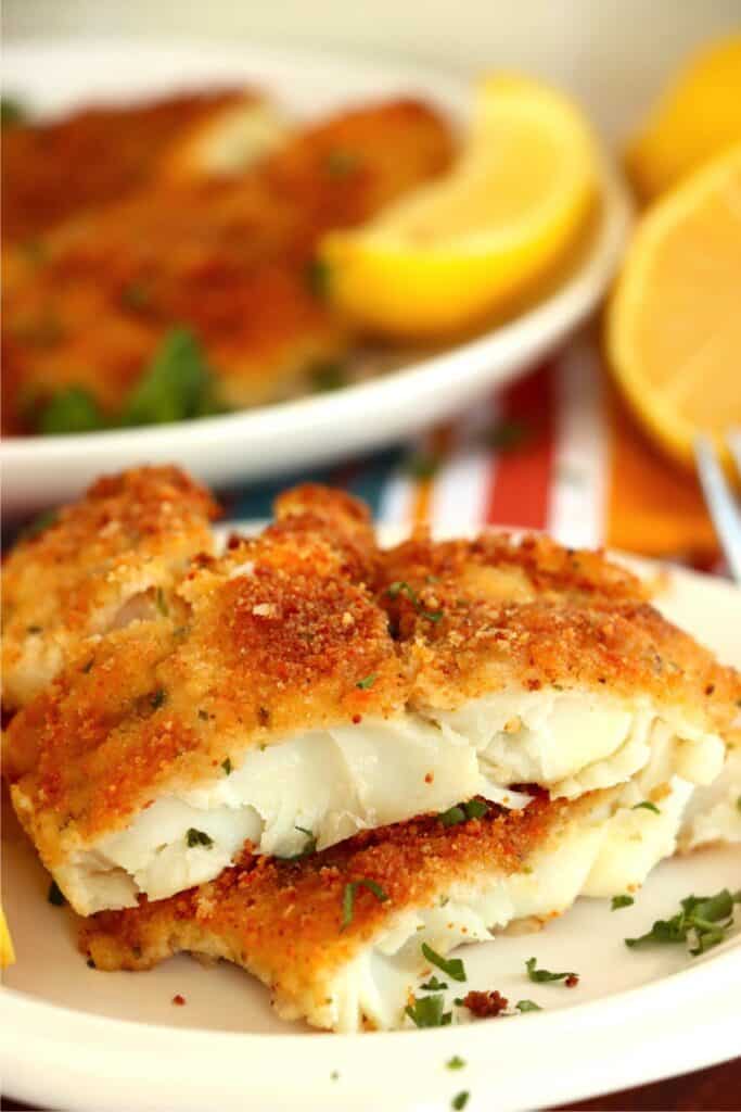 Closeup shot of parmesan crusted cod fillet halves stacked atop one another on plate. 