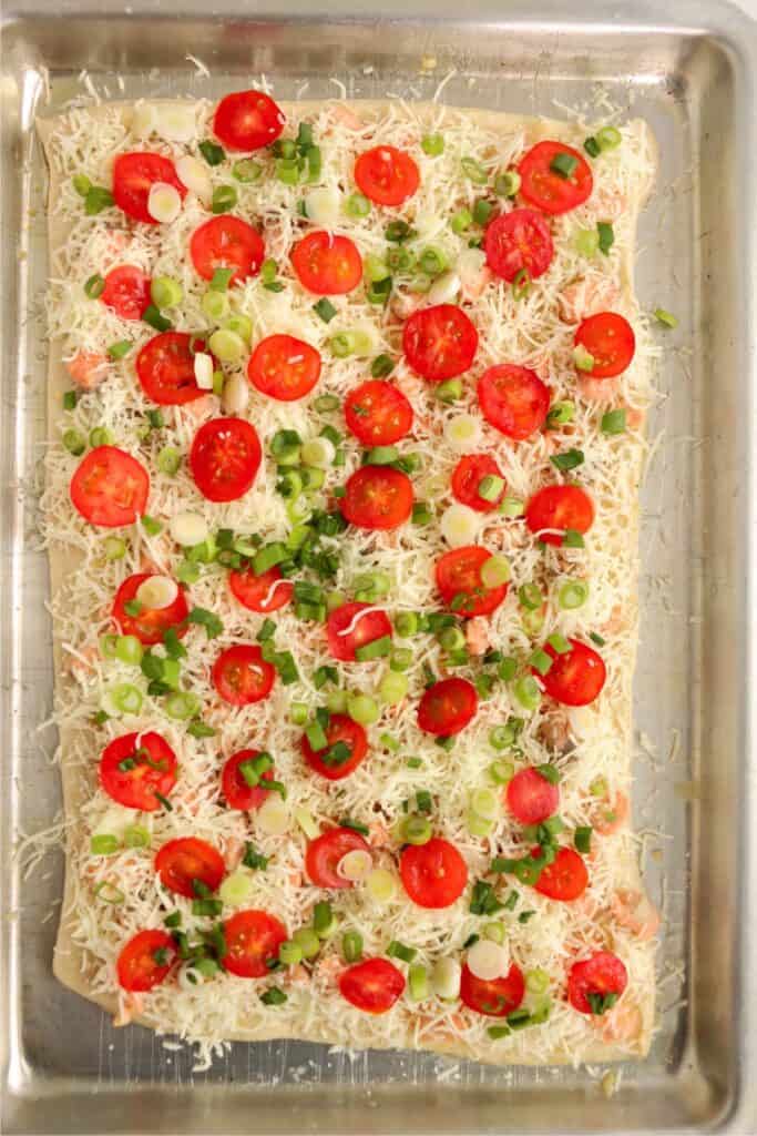 Overhead shot of salmon, cheese, tomatoes, and green onions on pizza crust.