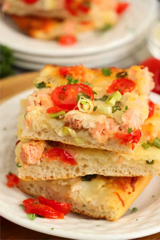 Closeup shot of three slices of salmon pizza stacked atop one another on plate. 