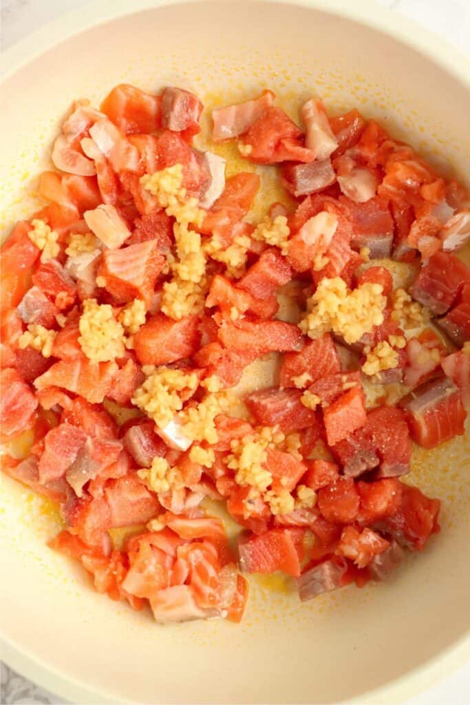 Overehead shot of raw salmon and minced garlic in skillet. 