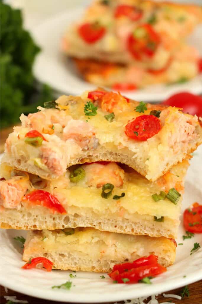 Closeup shot of three slices of salmon pizza stacked atop one another with bite taken out of the top slice. 