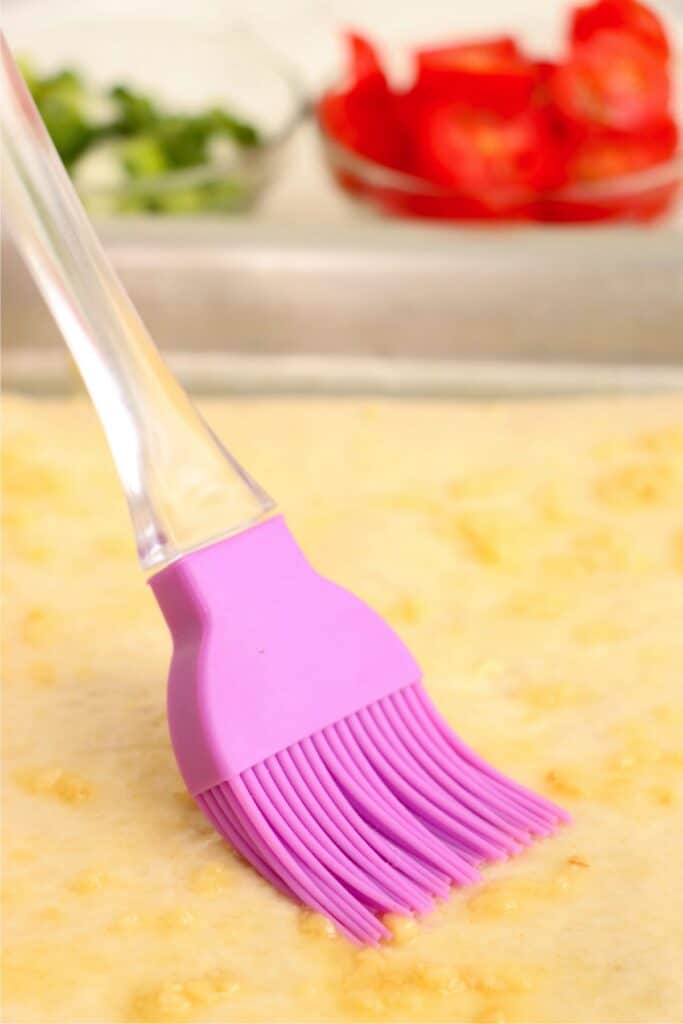 Closeup shot of garlic butter being brushed onto unbaked pizza crust. 