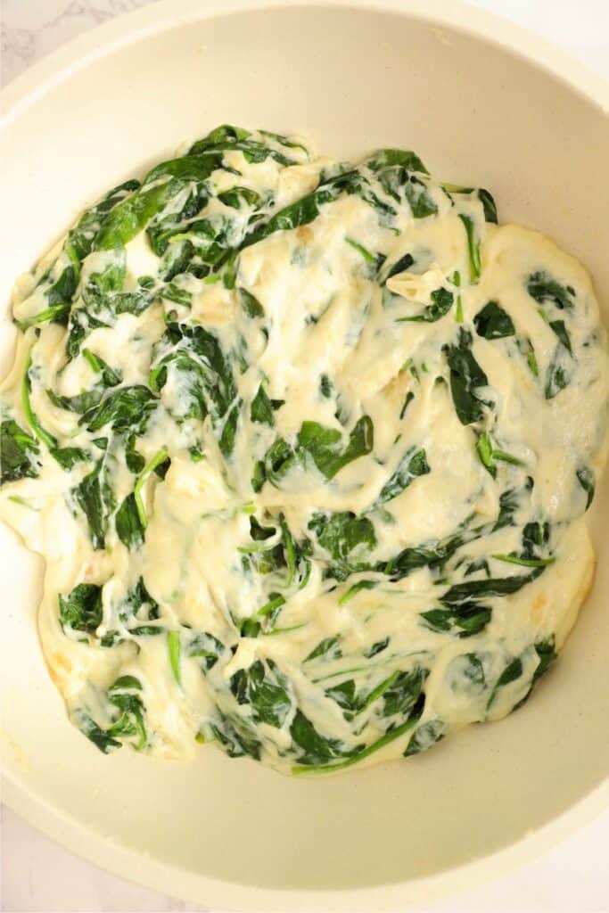 Overhead shot of wilted spinach and melted cheese in skillet. 