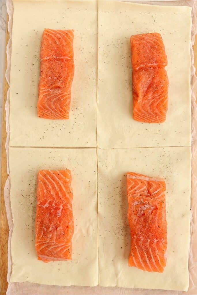Overhead shot of four puff pastry rectangles topped with a seasoned salmon fillet. 