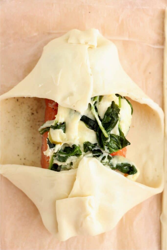 Closeup shot of spinach and cheese-topped salmon fillet being wrapped in puff pastry dough. 
