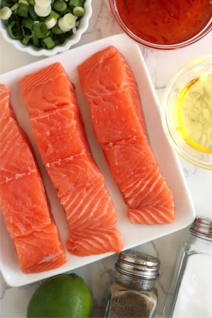 Overhead shot of plate with salmon fillets next to bowls of other ingredients