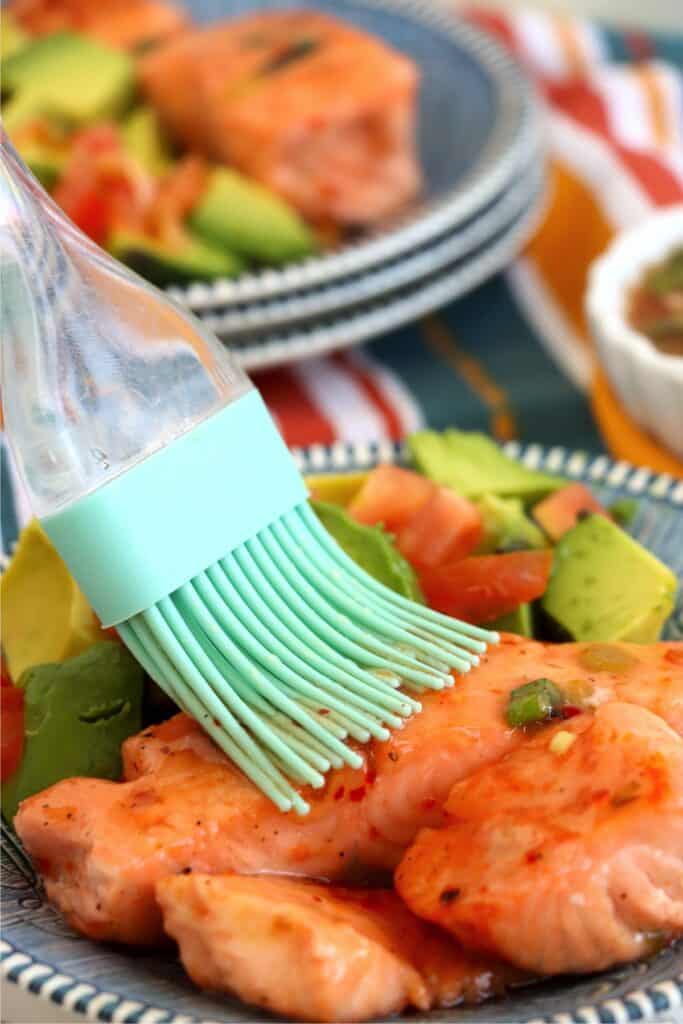 Closeup shot of sweet chili sauce being brushed over salmon fillets. 