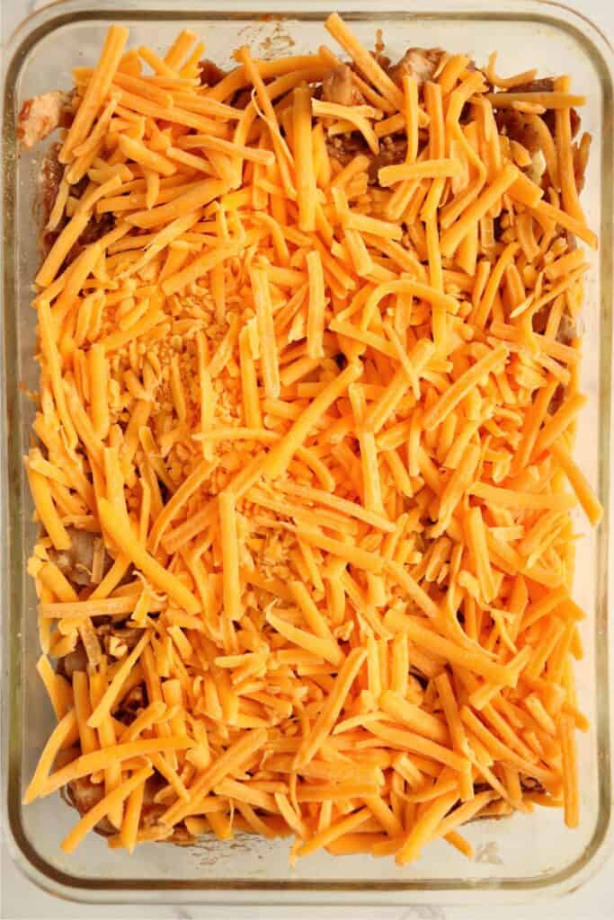 Overhead shot of Hawiian roll bottoms topped with shredded BBQ chicken and shredded cheddar cheese.