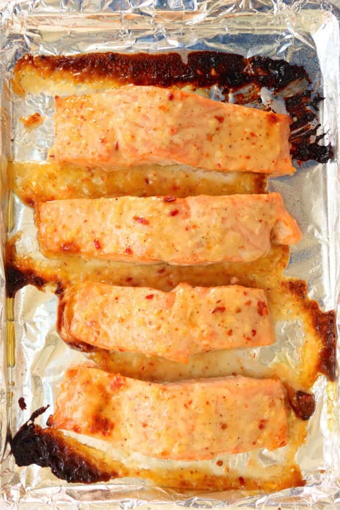 Overhead shot of baked salmon with mayonnaise on baking sheet.