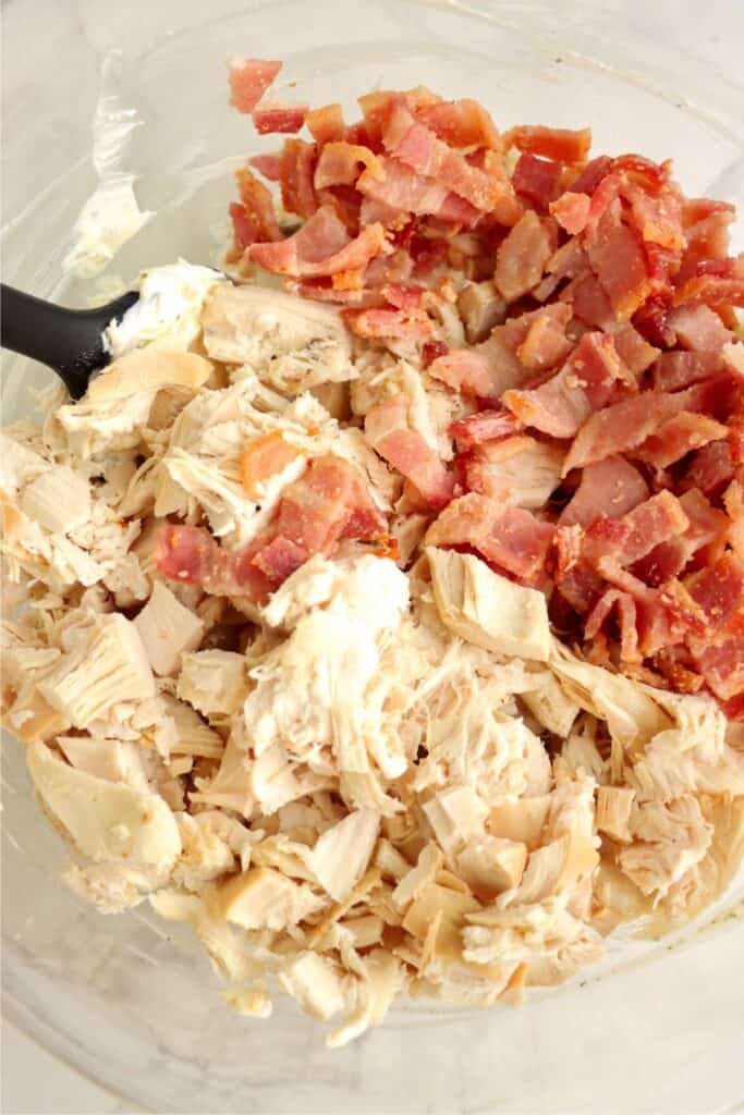Closeup shot of chicken and bacon being stirred into cream cheese mixture. 