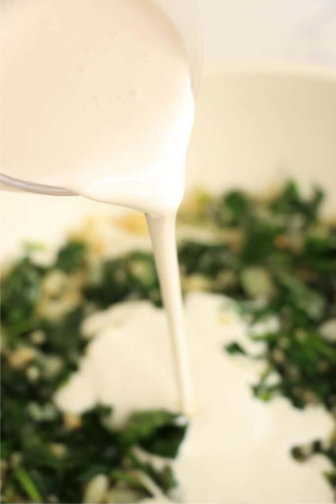 Heavy cream being poured into skillet full of spinach. 