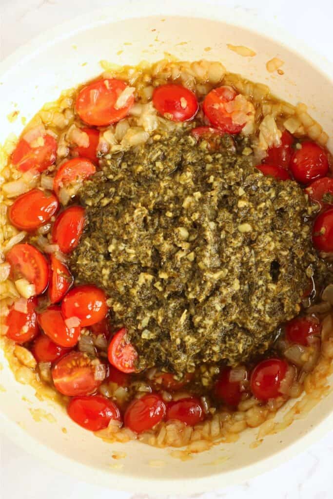 Overhread shot of pesto, tomatoes, onions, and garlic in skillet. 