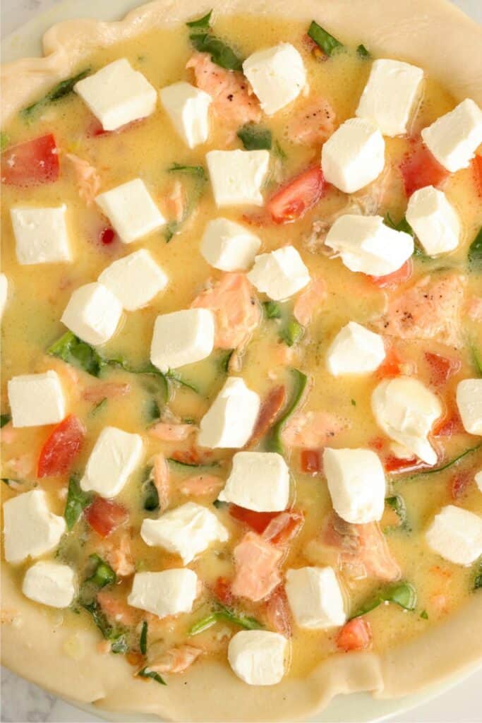 Overhead shot of uncooked spinach salmon quiche topped with cubed cream cheese. 