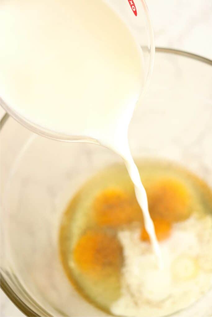 Overhead shot of milk being poured into bowlful of eggs. 