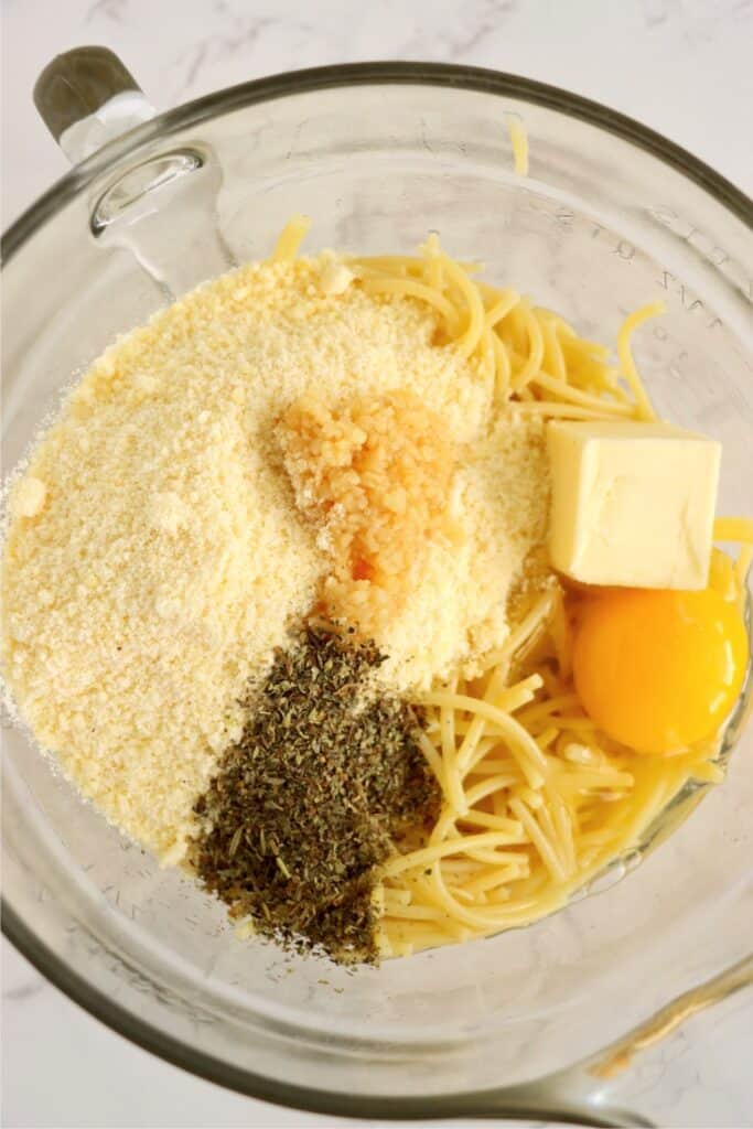 Overhead shot of spaghetti noodles, parmesan cheese, eggs, butter, and seasonings in bowl. 
