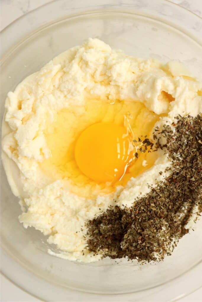 Closeup overhead shot of ricotta cheese, egg, and oregano. 