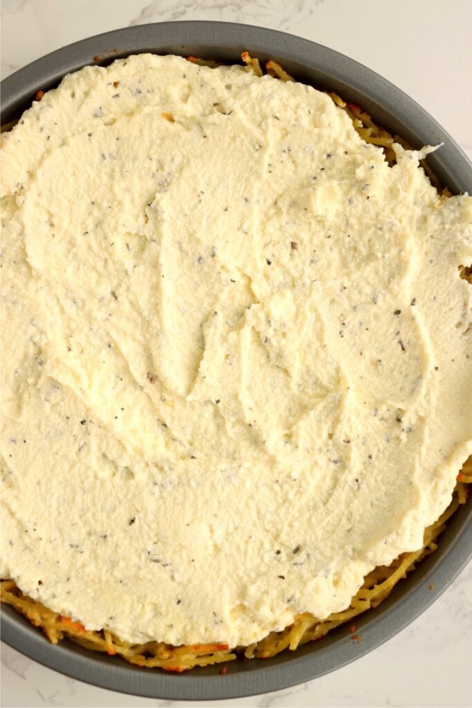 Overhead shot of spaghetti crust topped with ricotta cheese. 