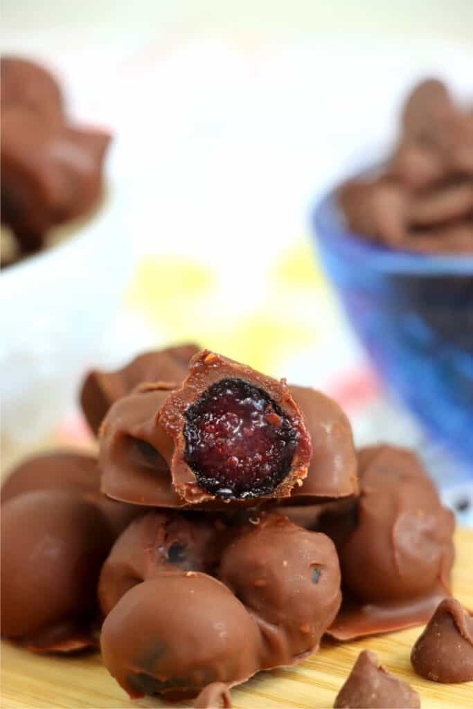 Closeup shot of pile of chocolate covered blueberry clusters with bite taken out of top cluster. 
