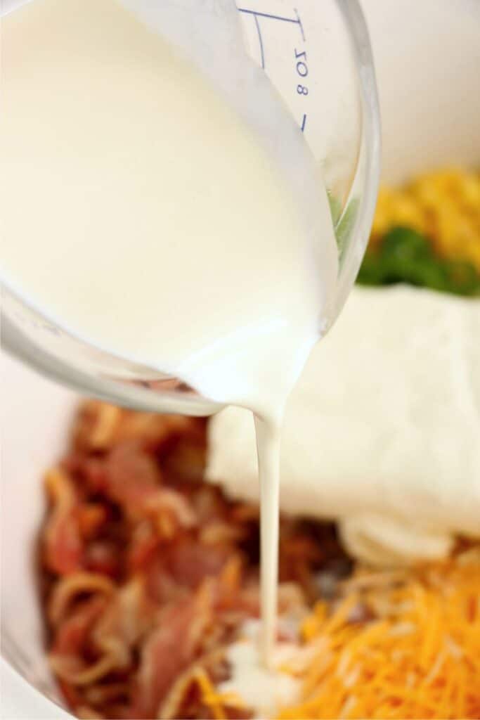 Closeup shot of cream being poured into crock pot full of cream corn ingredients.