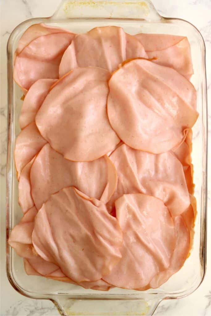 Overhead shot of baking dish full of Hawaiian roll bottoms topped with turkey slices. 