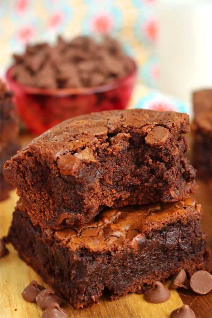 Closeup shot of two chocolate chip brownies stacked atop one another with bite taken out of top brownie. 