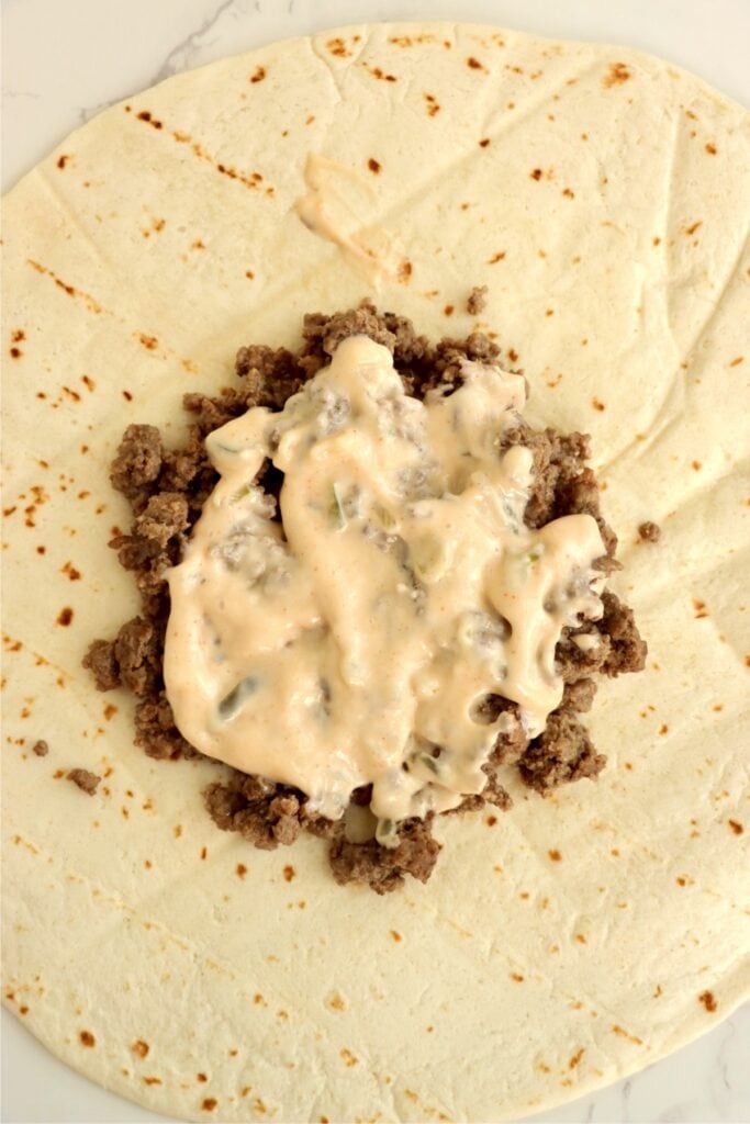 Overhead shot of ground beef topped with Big Mac sauce on tortilla. 