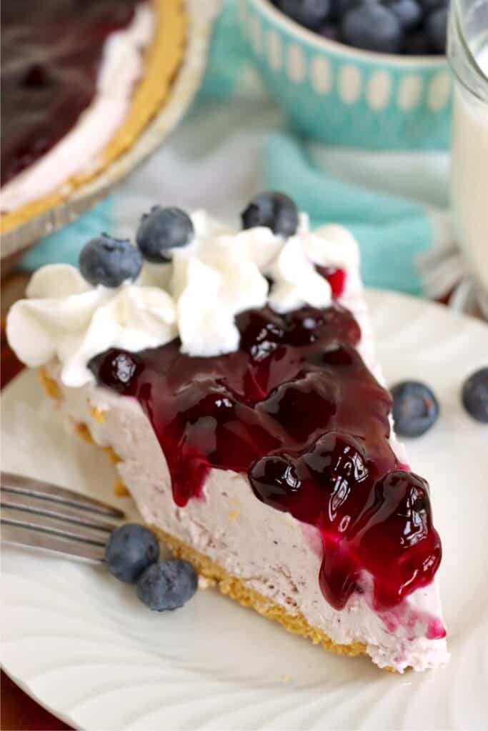 Slice of blueberry cream cheese pie topped with whipped cream and fresh blueberries. 